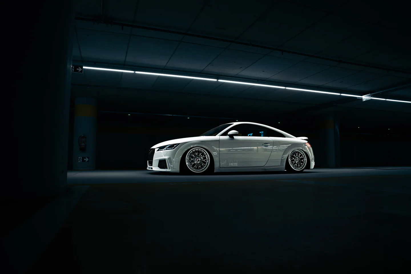 Witte Audi TT onder lijnverlichting in een donkere parkeergarage